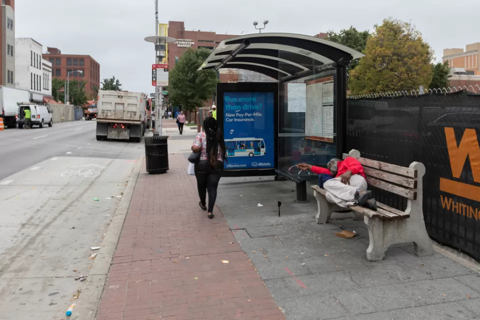 Unhoused person sleeping on bench at bus stop on Baltimore street